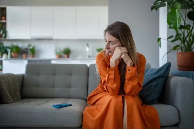 Mulher sentada no sofá desconfiada, com traumas do passado